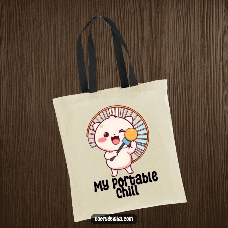 Funny tote bag shows a small, round Kawaii character holding a large fan, perfect for carrying essentials.